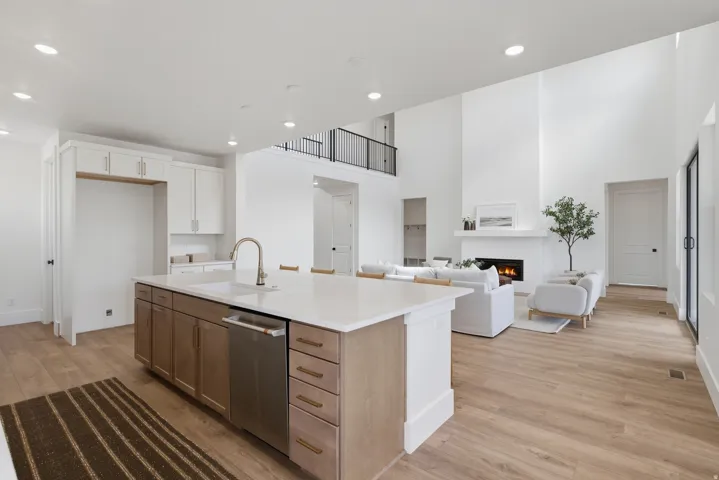 Open-concept living space with wood-finish flooring, a kitchen island with integrated sink, a fireplace, and an upper-level balcony with black railing