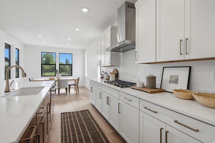 Well-appointed kitchen featuring a gas range, stainless steel range hood, white cabinetry, integrated sink, and light-toned flooring