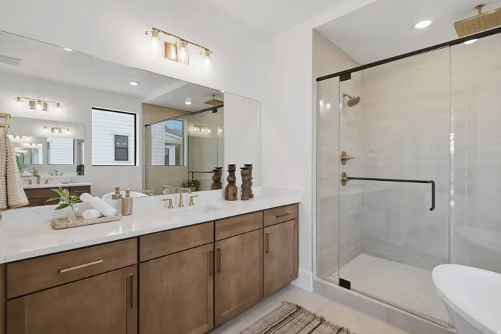 Dual vanity with white countertop, recessed lighting, and a glass-enclosed shower featuring a rain shower head