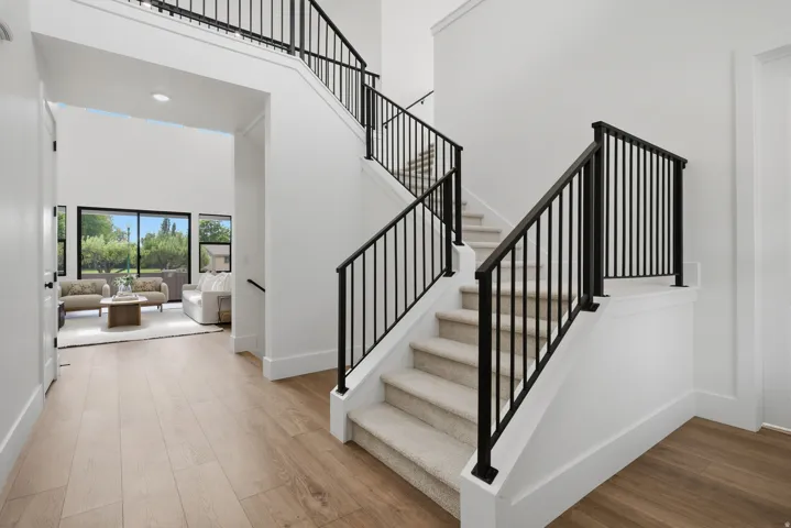 Two-story entryway featuring LVP flooring, a carpeted staircase with black iron railings, and a double-height ceiling