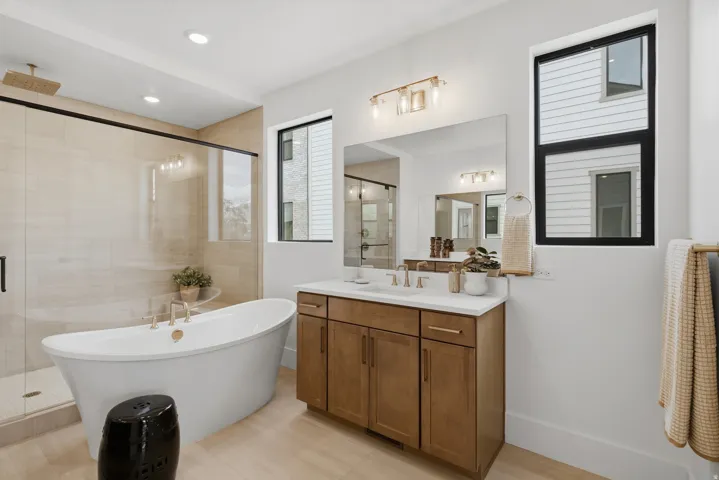 Freestanding soaking tub with brass fixtures, glass-enclosed shower with a rainfall showerhead, and dual vanity with undermount sinks