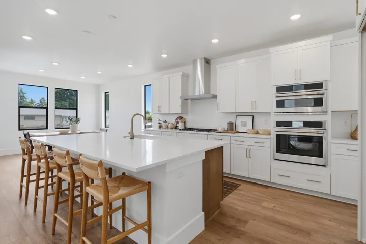 Expansive kitchen featuring a large central island with seating, white shaker cabinetry, stainless steel appliances, and LVP flooring