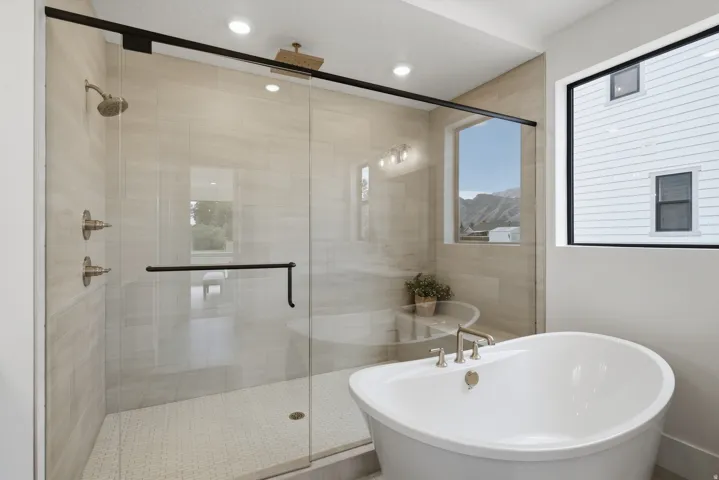 Freestanding soaking tub with brushed nickel fixtures, glass-enclosed shower with a rainfall showerhead, and tiled walls