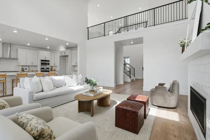 Expansive living area with high ceilings, featuring LVP flooring, a contemporary fireplace, and an open concept kitchen with white cabinetry and stainless steel appliances
