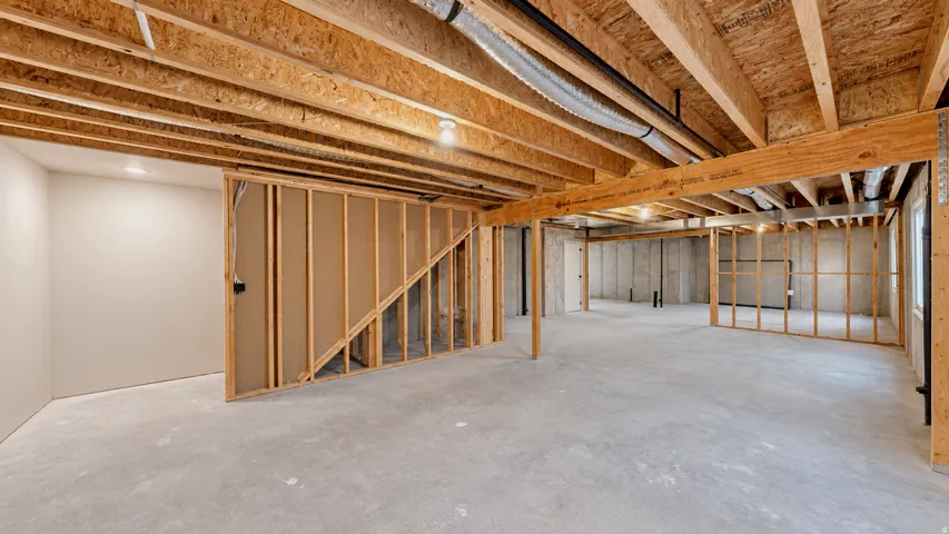 Unfinished lower level with concrete flooring, exposed wood joists, and framed partition walls