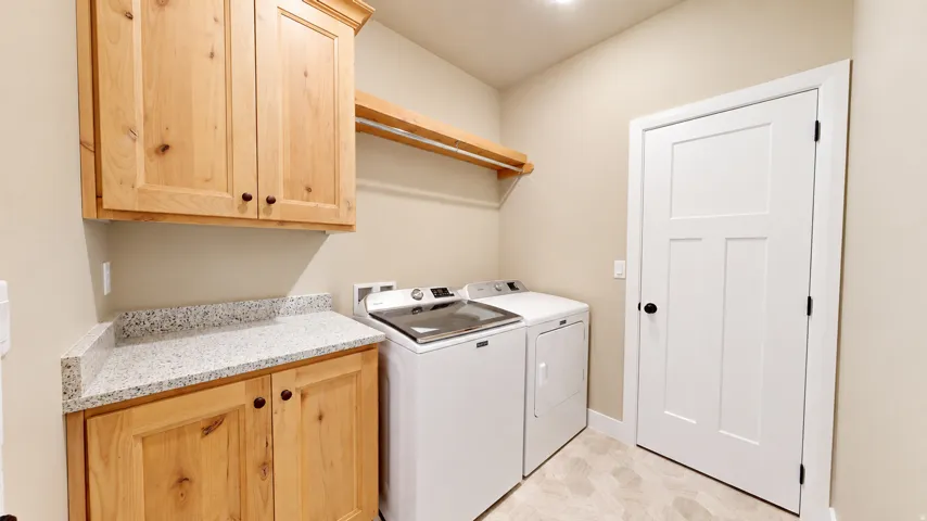 Light wood cabinetry with black hardware, light-toned countertop, wood-finish flooring, and a white interior door with black hardware