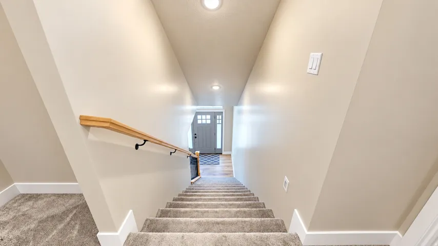 Carpeted staircase with a wood-finish handrail and white trim