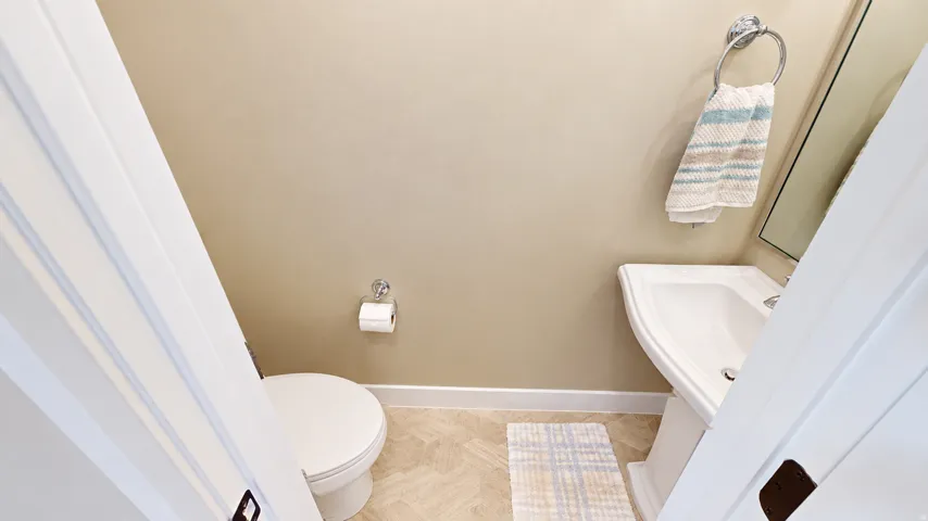 Pedestal sink with chrome faucet, toilet, and light-toned flooring