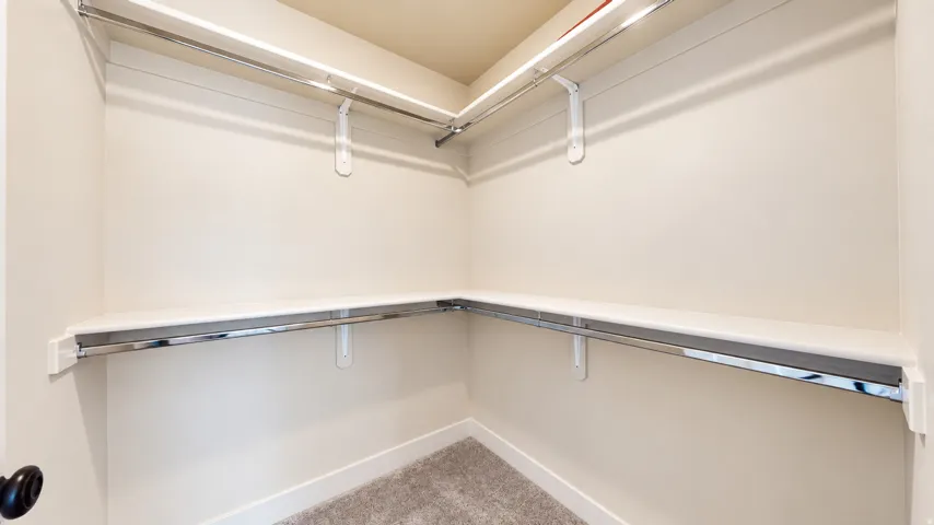 L-shaped shelving with chrome hanging rods, light-toned walls, and carpet flooring