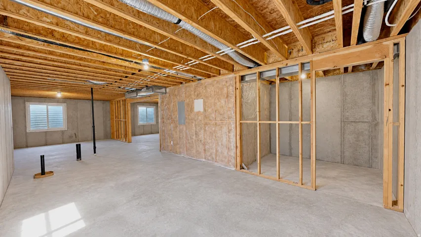 Unfinished basement featuring exposed wood joists, concrete floor, framed interior walls, and horizontal windows