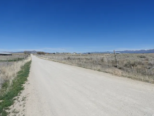 Expansive rural setting with a clear blue sky, distant mountains, and an unpaved road