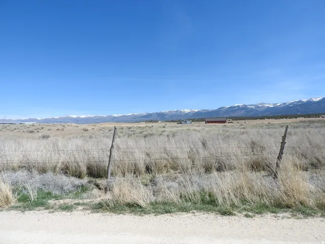 Expansive open land with a distant red outbuilding, post and wire fencing, and a mountainous backdrop