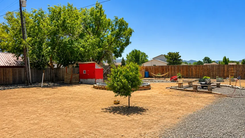 Expansive backyard featuring a gravel patio, wood privacy fencing, mature trees, and a red shed
