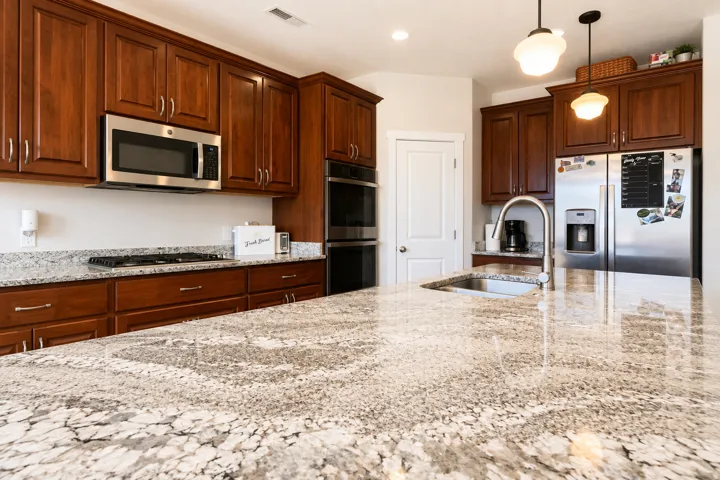 Kitchen featuring stone countertops, dark wood-finish cabinetry, stainless steel appliances, and an undermount sink with a gooseneck faucet