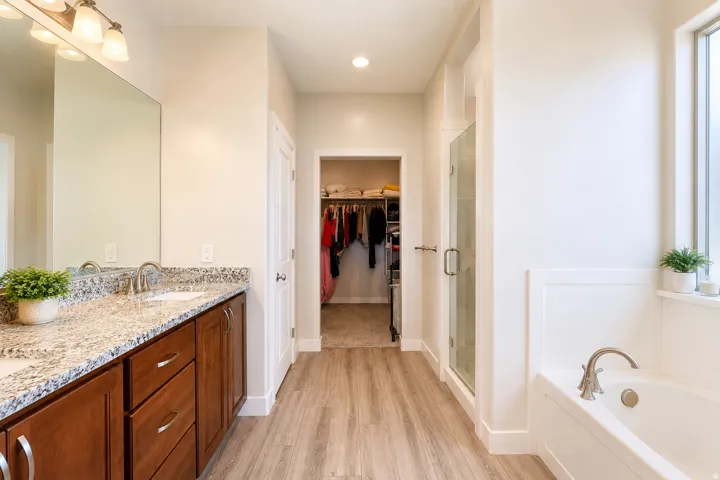 Dual vanity with granite countertop, wood-finish flooring, glass-enclosed shower, built-in bathtub, and recessed lighting