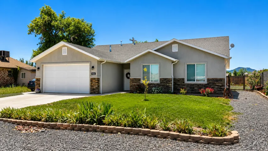 Stucco exterior with stone accent detailing, attached two-car garage, concrete driveway, and front lawn