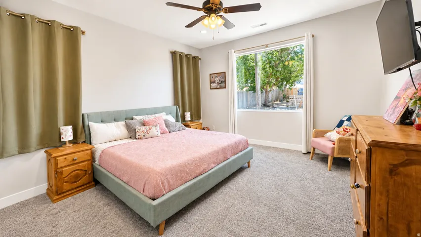 Carpeted flooring, ceiling fan, and a large window with white trim