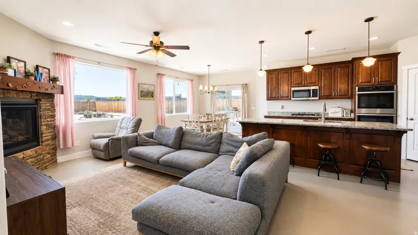 Open-concept living area featuring a stacked stone fireplace, large windows, and a ceiling fan