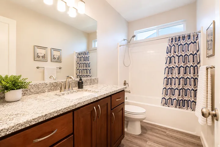 Wood-finish flooring, a vanity with a light-colored countertop, and a shower-tub combination