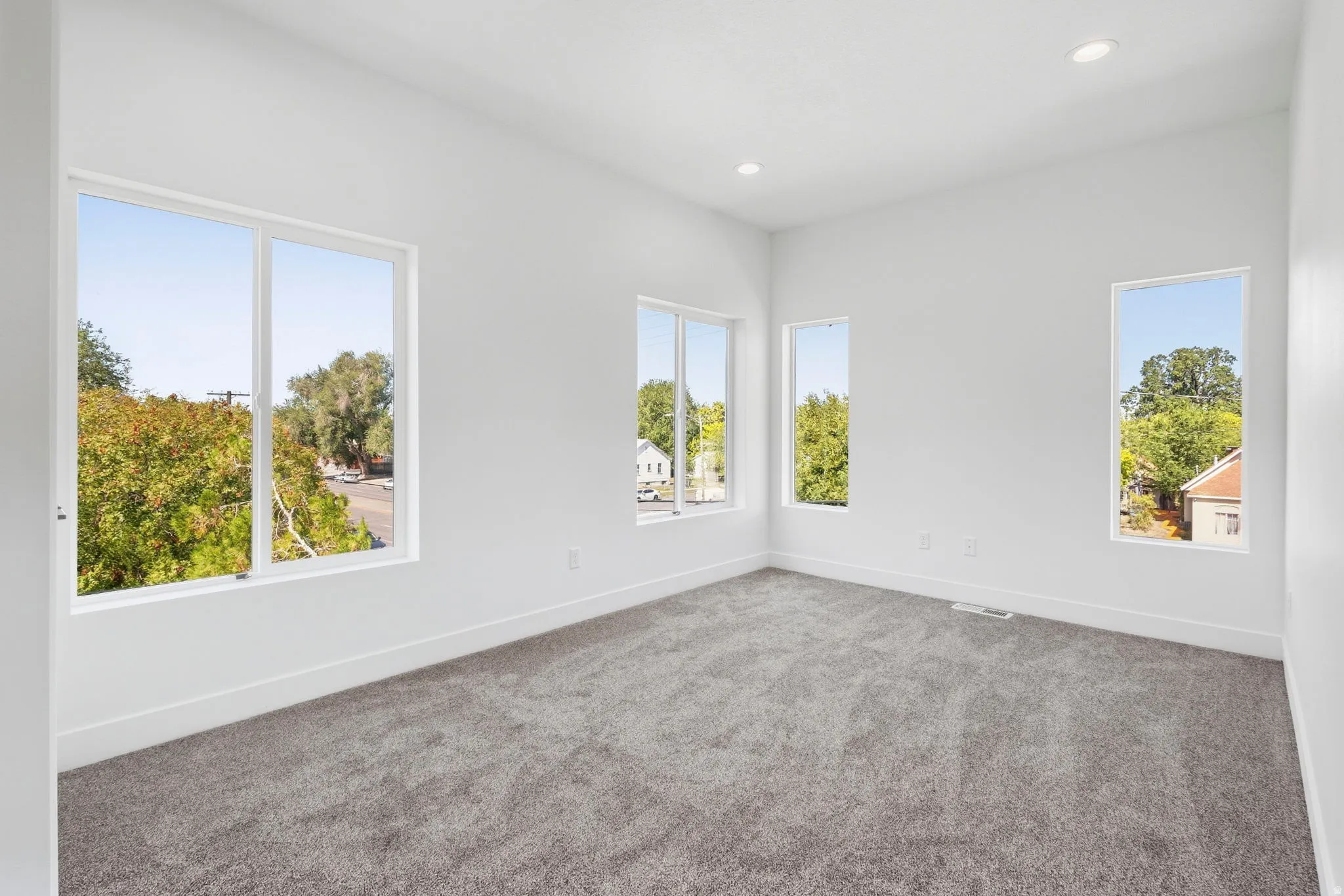 White interior walls, gray carpeting, multiple large windows, and recessed lighting