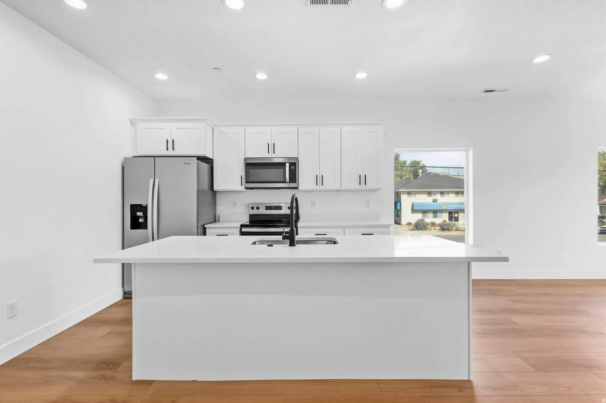Modern kitchen featuring white shaker cabinetry, stainless steel appliances, a center island with a white countertop, and wood-finish flooring
