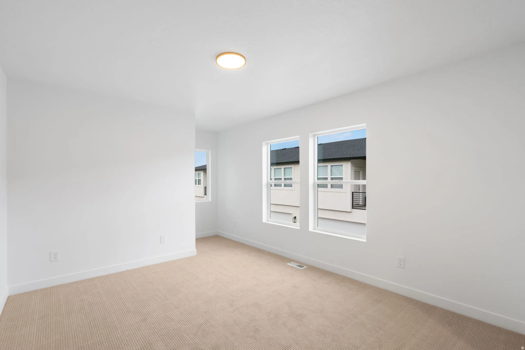 Recessed lighting, three windows providing natural light, neutral carpeting, and white wall finishes