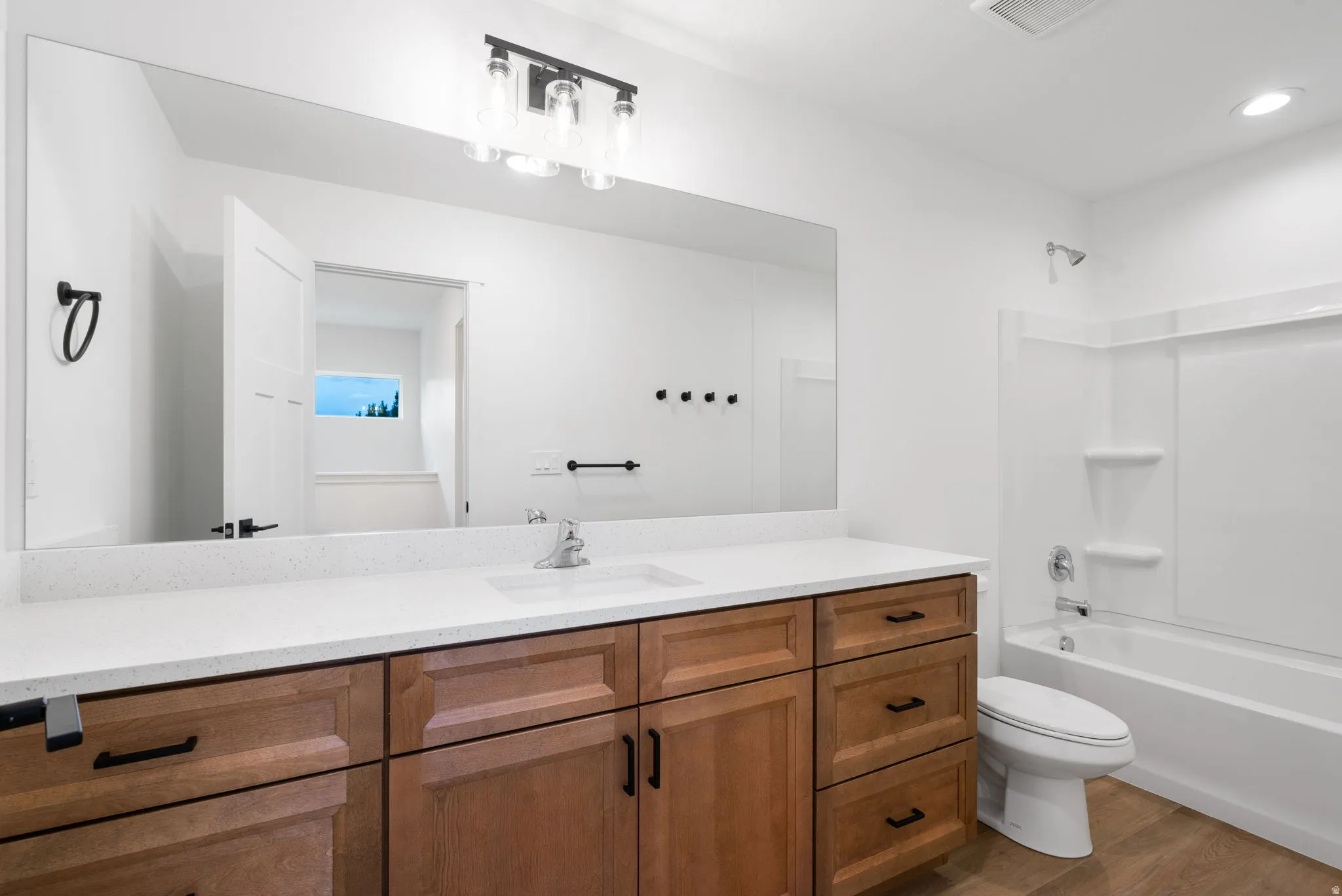 Wood-finish flooring, extensive countertop space with integrated sink, wood cabinetry, and a full-size bathtub with shower