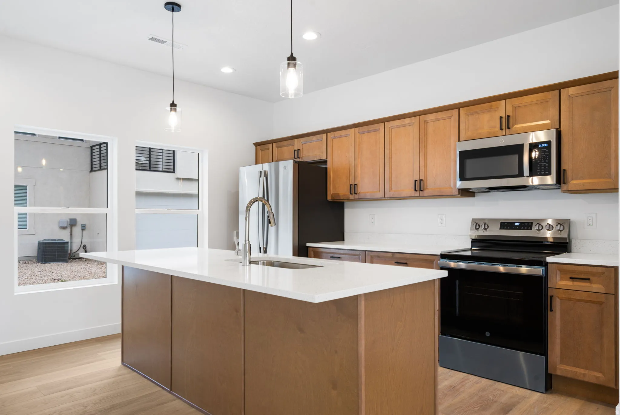 Kitchen featuring a center island with sink, stainless steel appliances, wood-finish cabinetry, and light-toned countertops
