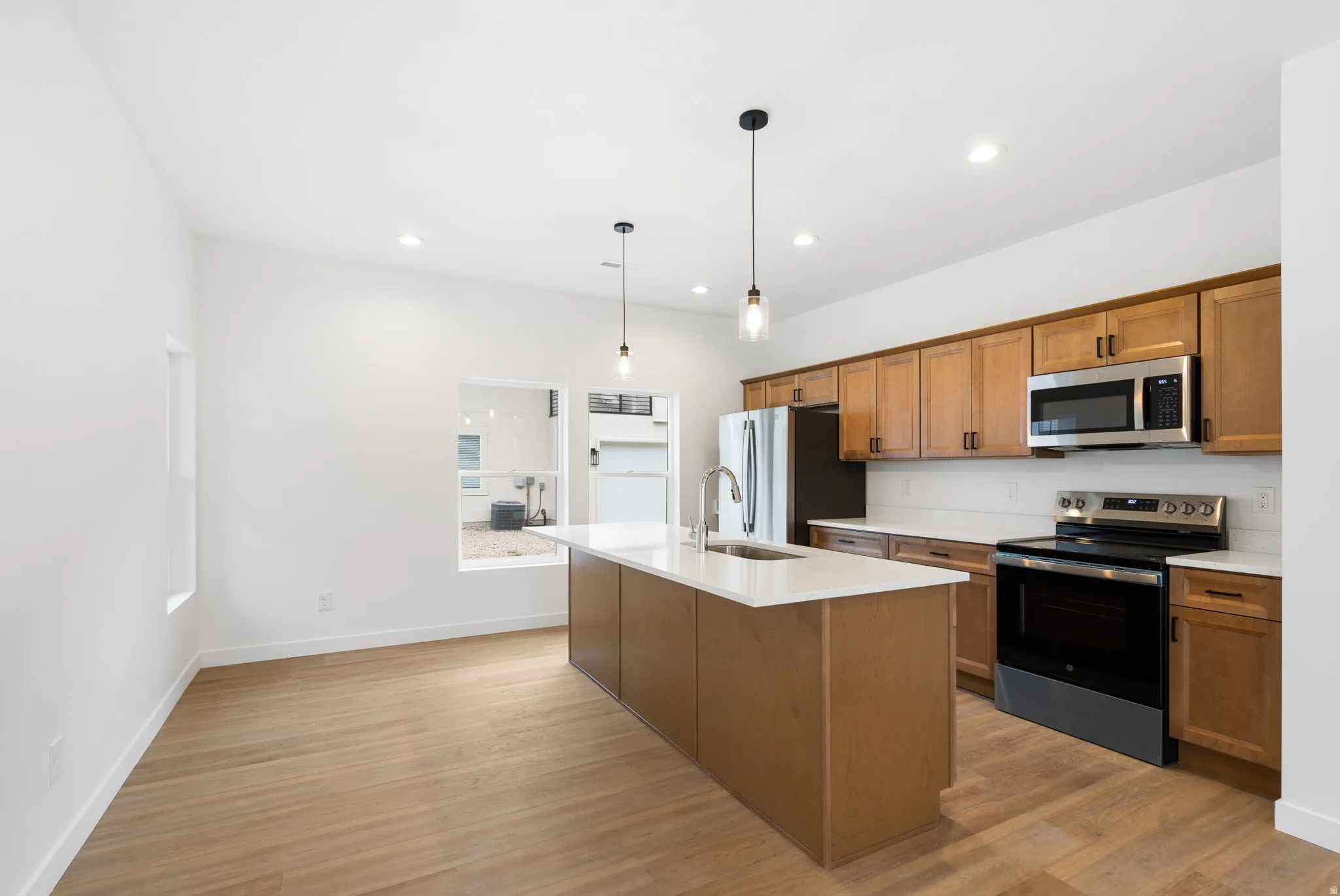 Kitchen featuring wood-finish flooring, an island with a sink, pendant lighting, stainless steel appliances, and wood cabinetry