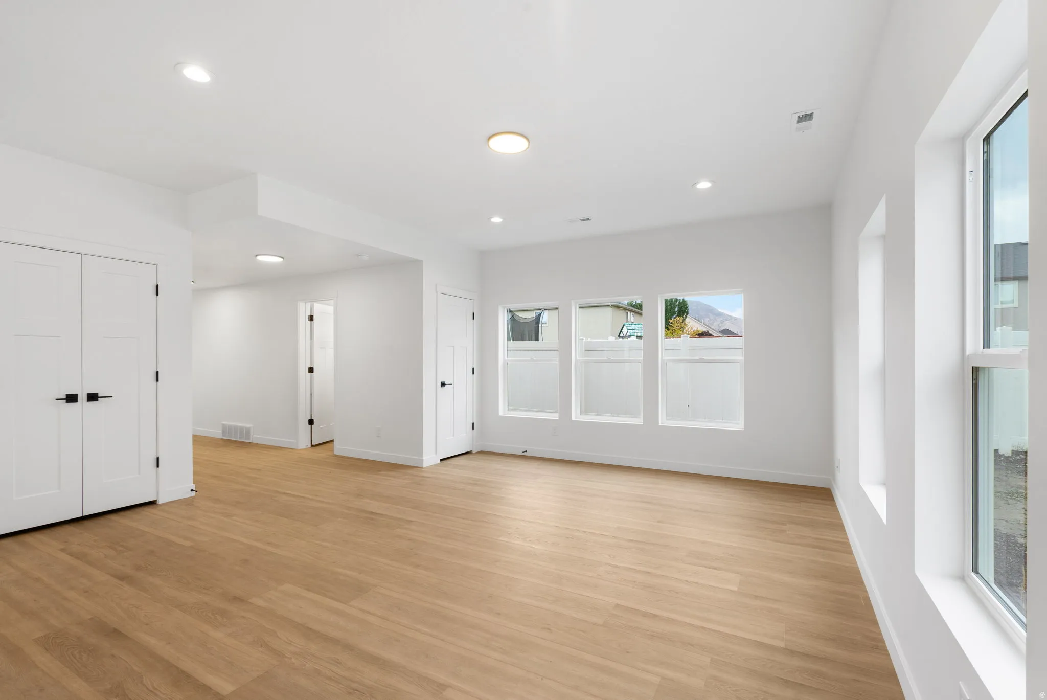 Recessed lighting, wood-finish flooring, white walls, multiple windows, and crisp white trim