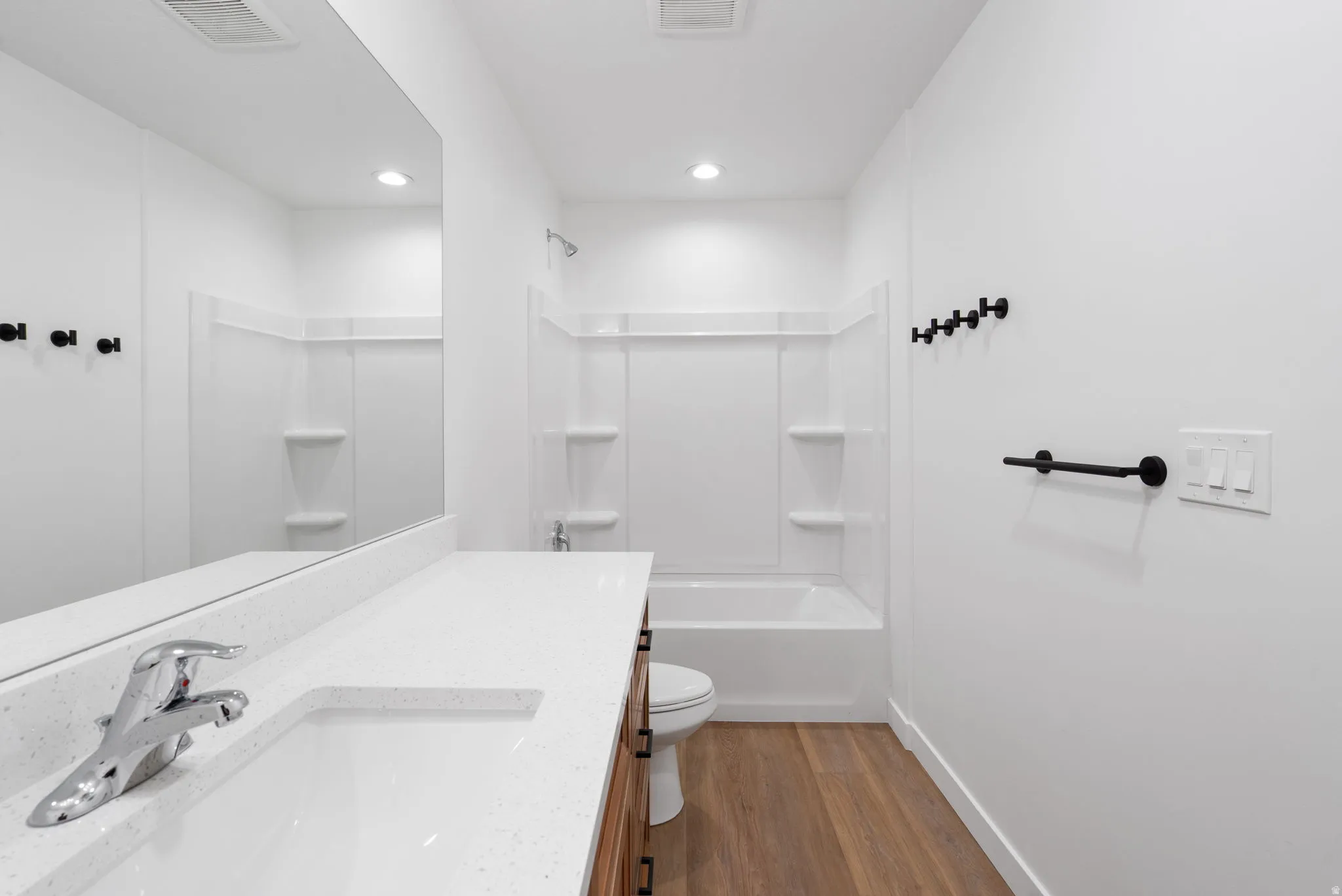 White bathroom featuring a built-in tub with white surround, wood-finish flooring, a vanity with a white countertop and integrated sink, and black hardware