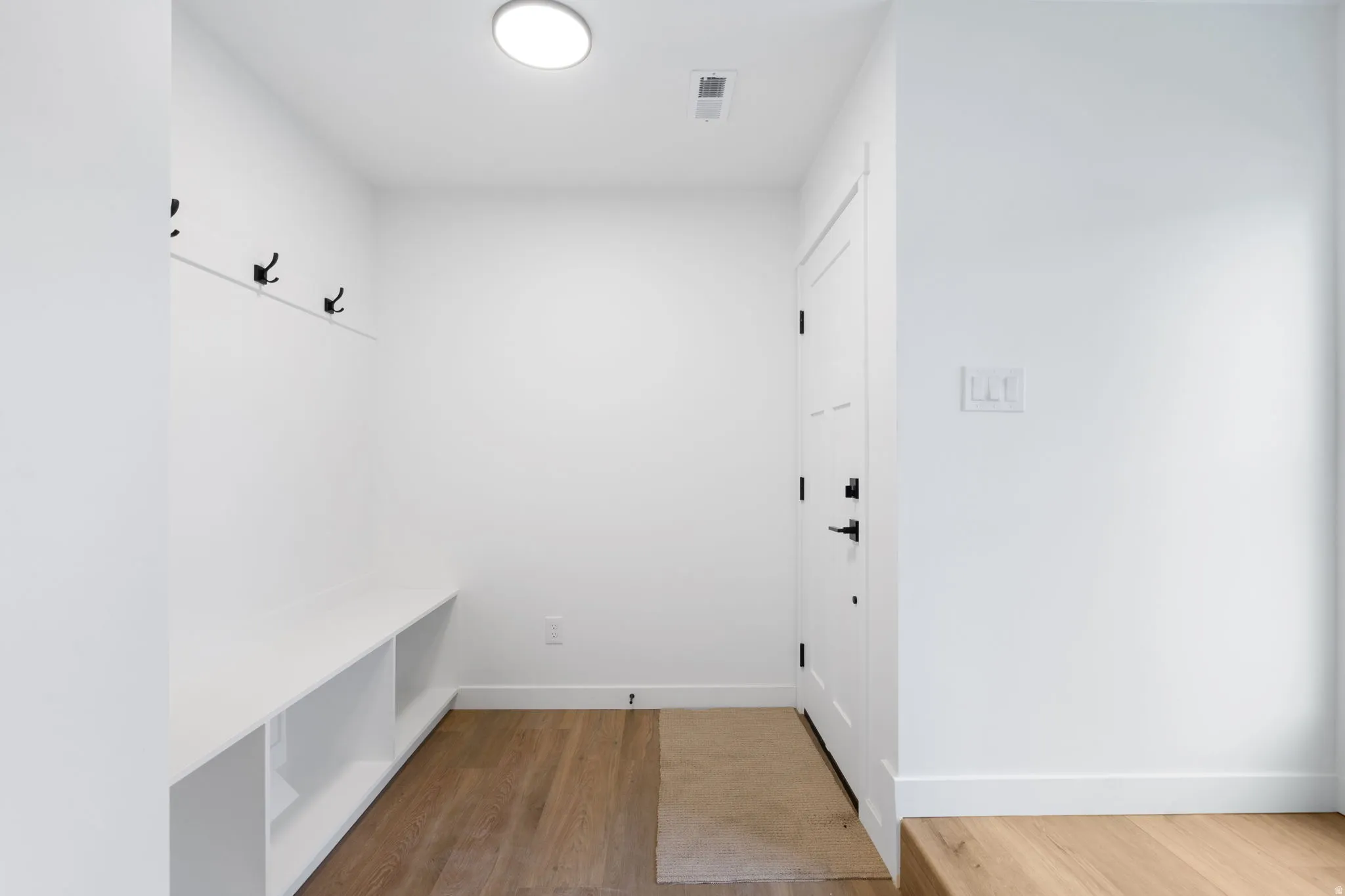 Entryway featuring wood-finish flooring, built-in bench with storage, wall-mounted coat hooks, and a contemporary flush-mount light fixture