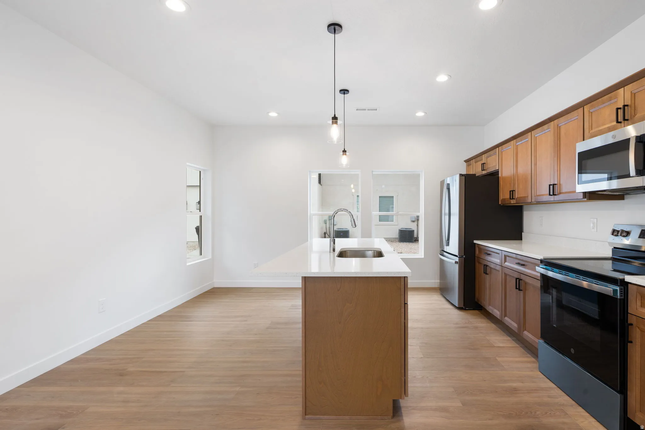 Open-concept kitchen featuring wood-finish flooring, recessed lighting, a kitchen island with sink, and stainless steel appliances