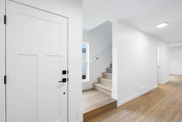 White paneled door with matte black hardware, wood-finish flooring, a carpeted staircase with a white handrail, and a recessed ceiling light fixture