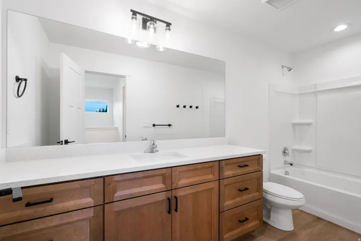 Wood-finish flooring, extensive countertop space with integrated sink, wood cabinetry, and a full-size bathtub with shower