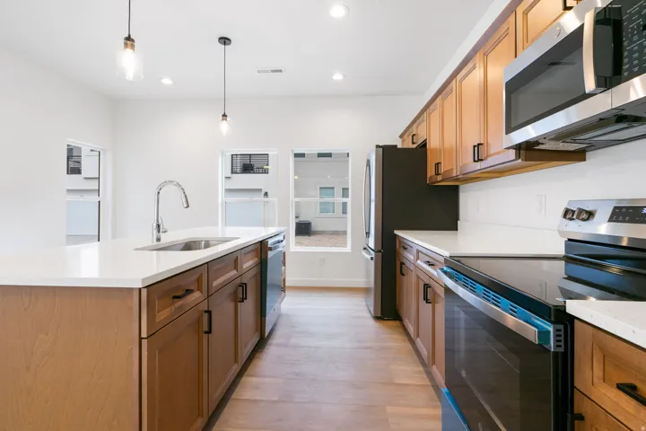 Open-concept kitchen featuring light wood-finish cabinetry, stainless steel appliances, white countertops, and wood-finish flooring