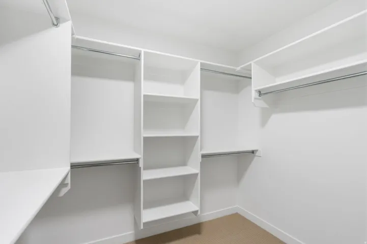 Spacious walk-in closet featuring white built-in shelving, multiple hanging rods, and light-colored carpeting