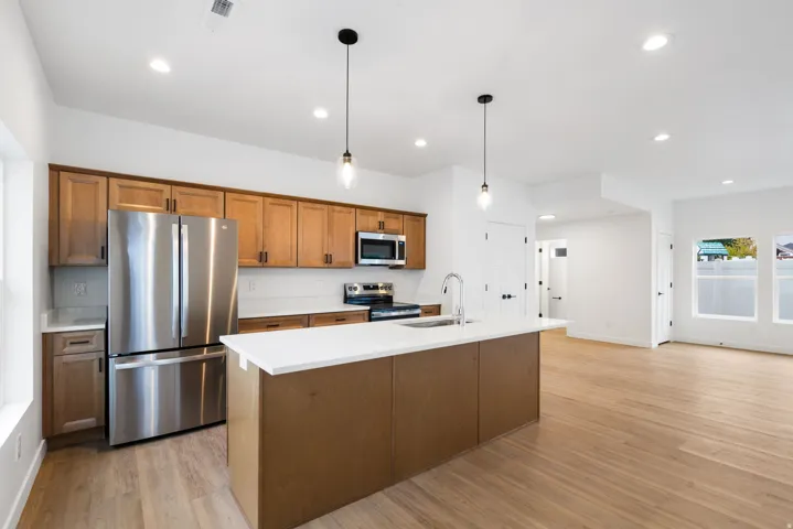 Kitchen featuring stainless steel appliances, wood-finish cabinetry, a central island with a sink, white countertops, and wood-finish flooring