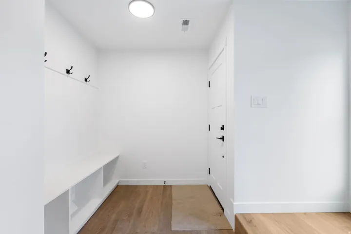 Entryway featuring wood-finish flooring, built-in bench with storage, wall-mounted coat hooks, and a contemporary flush-mount light fixture