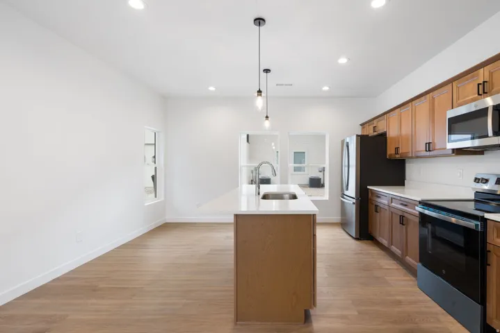 Open-concept kitchen featuring wood-finish flooring, recessed lighting, a kitchen island with sink, and stainless steel appliances