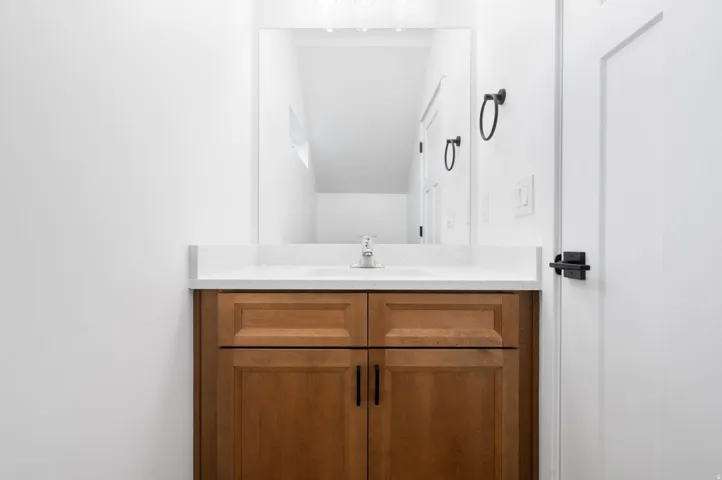 Wood-finish vanity with paneling and black hardware, white countertop, and integrated rectangular sink with chrome faucet