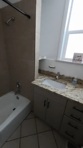 Bathroom featuring a tiled shower surround, built-in bathtub, vanity with an integrated sink, stone-finish countertop, and tile flooring