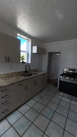 Kitchen with tiled flooring, light-toned cabinetry, a stainless steel range, and a window above the sink
