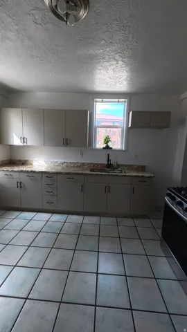 White cabinetry with black hardware, granite-look countertops, stainless steel sink with a black faucet, and tiled flooring