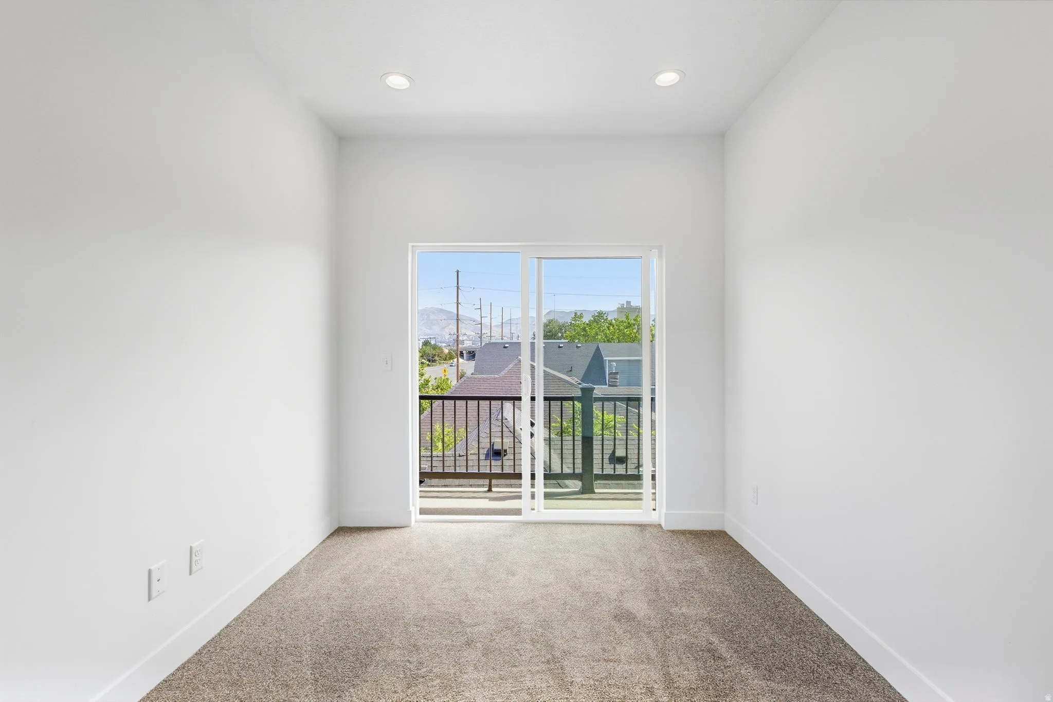 Recessed ceiling lighting, white walls, light-toned carpeting, glass sliding door, and a black metal balcony railing