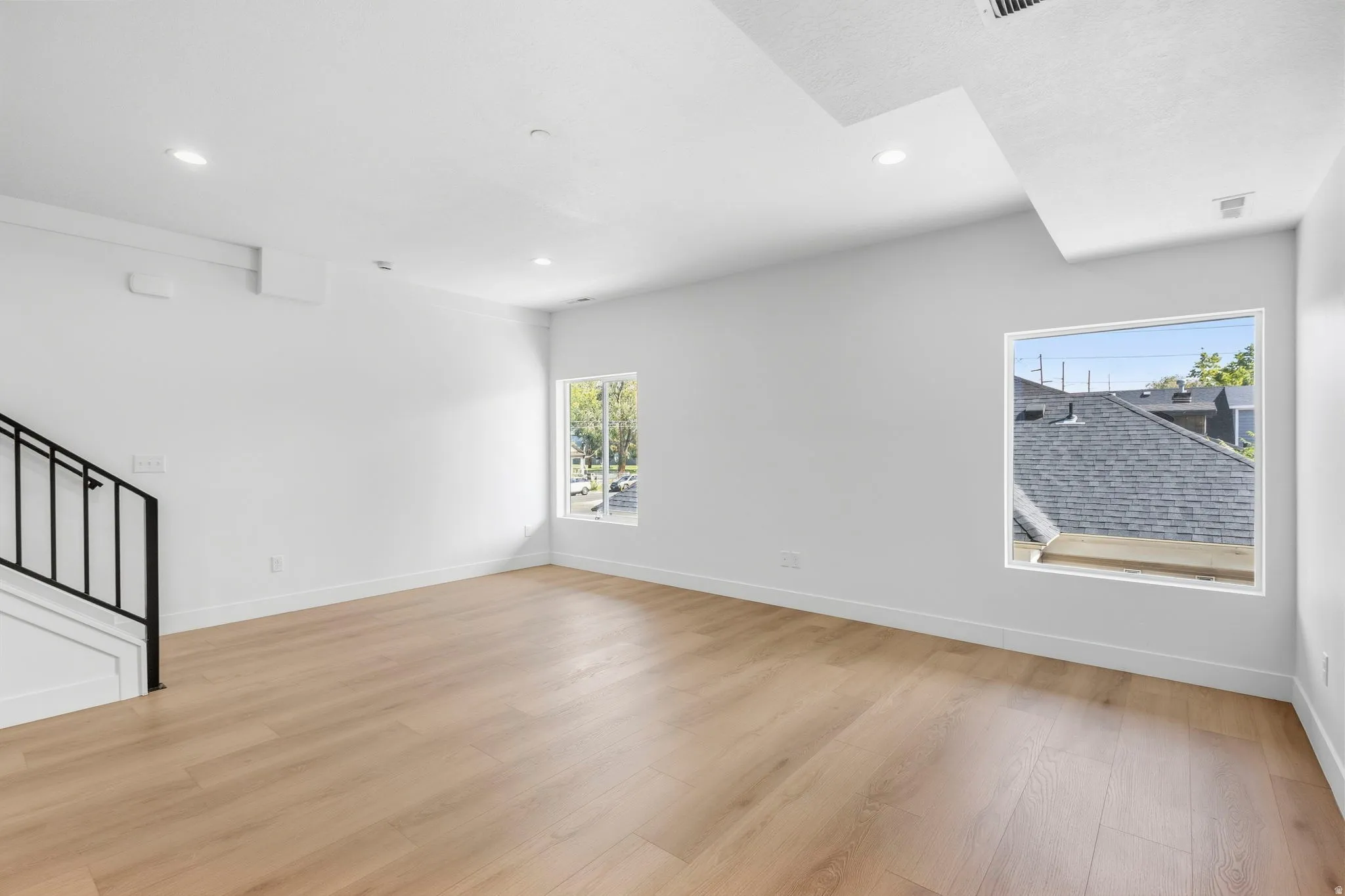 Recessed lighting, wood-finish flooring, white walls, black metal staircase railing, and multiple windows