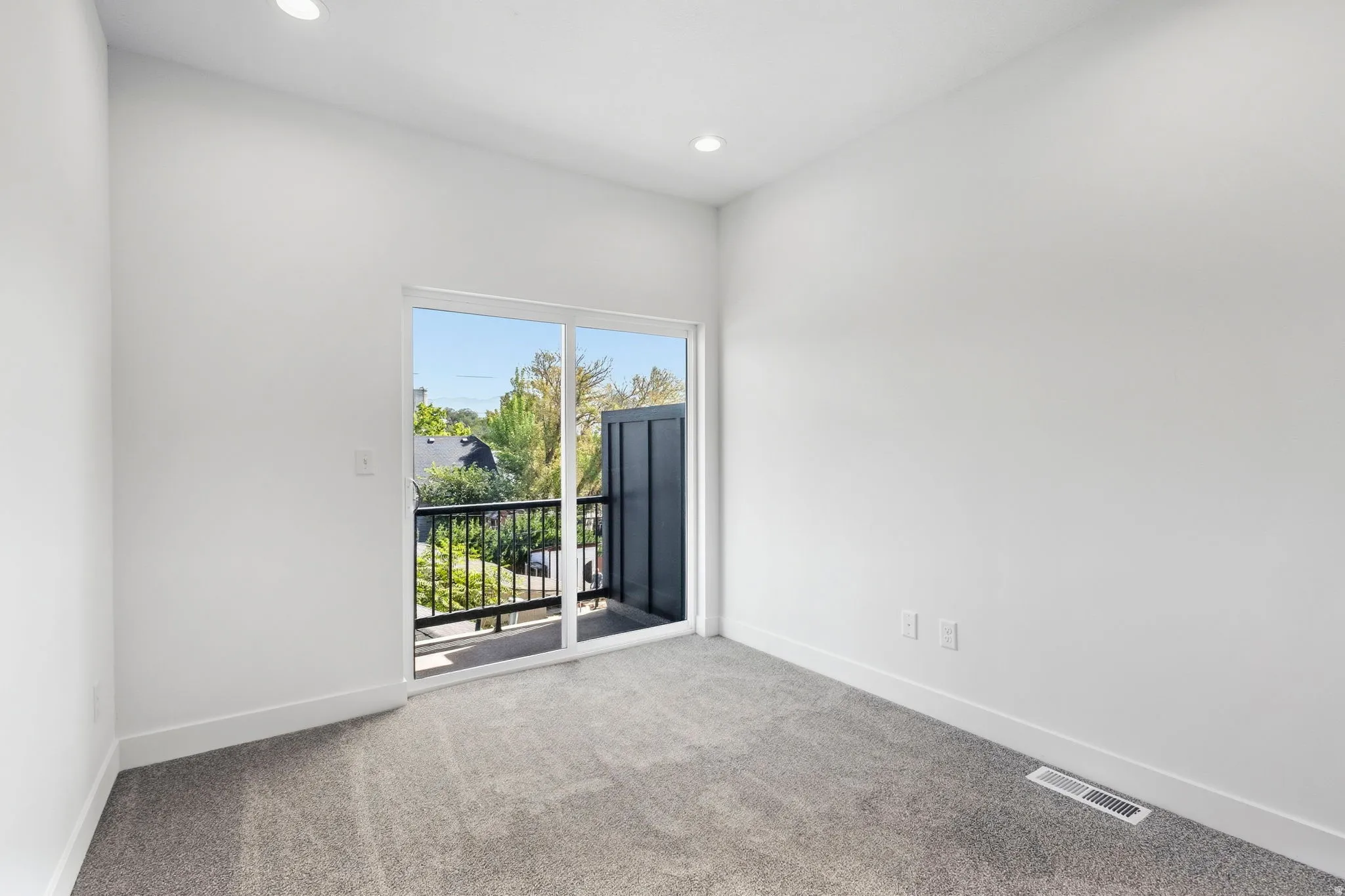 Carpeted room with recessed lighting and a sliding glass door leading to a balcony with black metal railings