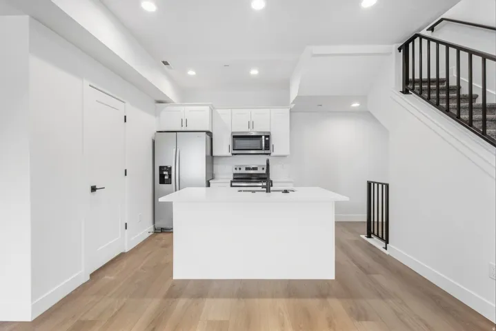 Contemporary kitchen featuring white cabinetry, a central island with a sink, stainless steel appliances, and wood-finish flooring
