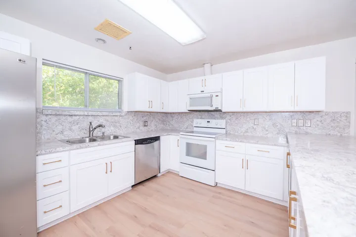 White cabinetry with gold-tone hardware, light-toned countertops, stainless steel sink, wood-finish flooring, and a built-in microwave