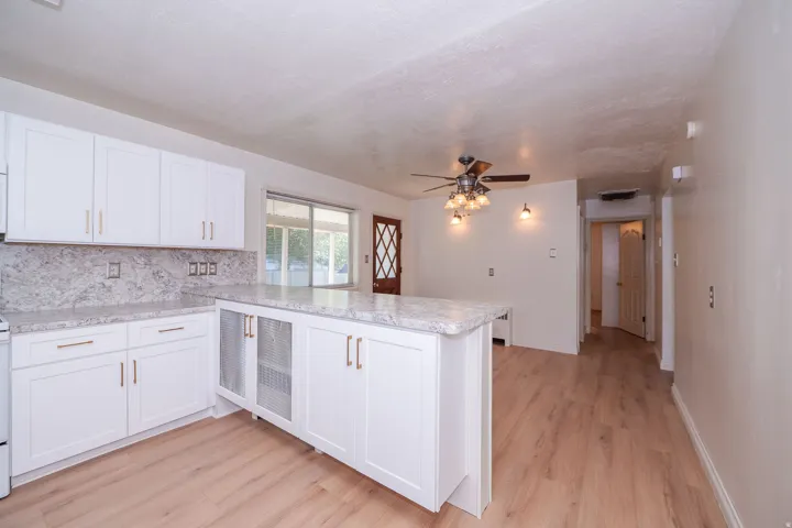 White shaker-style cabinetry with gold-finish hardware, granite-finish countertops, wood-finish flooring, a ceiling fan with integrated lighting, and a sliding glass door